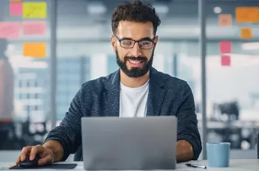 Business Mann sitzt vor Laptop und arbeitet im Büro