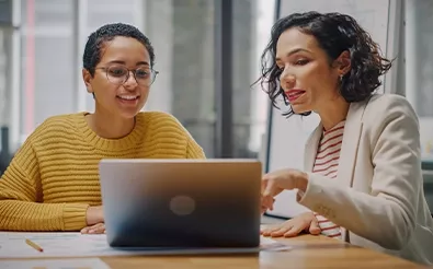 Zwei Business Frauen sitzen vor einem Laptop und setzen ihr Wissen aus dem E-Commerce Studium ein