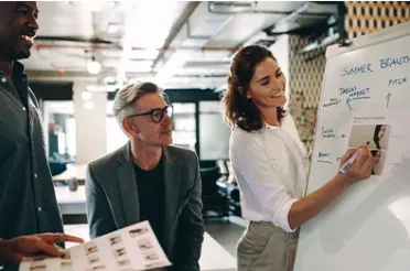 Zwei Männer und eine Frau stehen vor einem Whiteboard und unterhalten sich