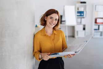 Eine Businessfrau hält einen Ordner in der Hand und lacht in die Kamera