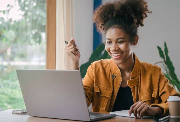 Eine Studentin sitzt lachend vor ihrem Laptop