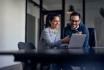 Eine Frau und ein Mann sitzen im Büro vor einem Laptop