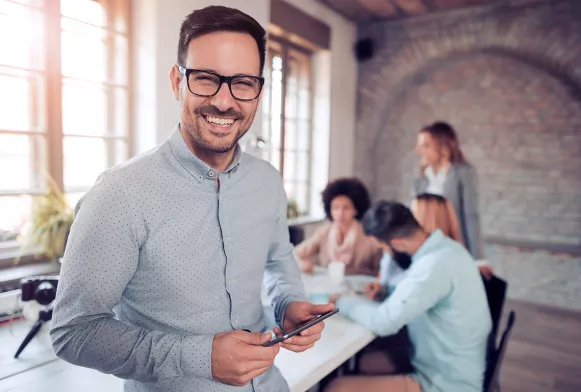 Mann im Businesslook hält Handy in der Hand und lächelt in die Kamera